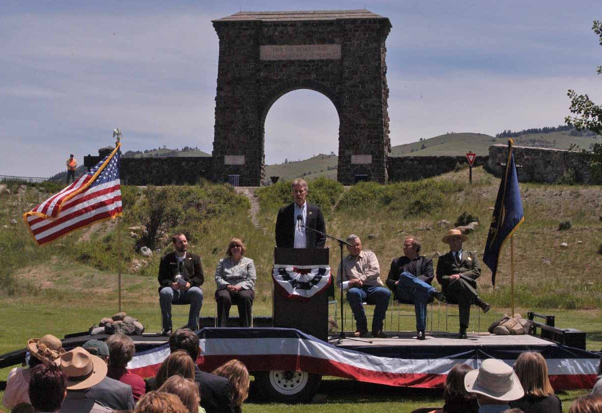 Bill Berg, president of the Greater Gardiner Community Council, speaks in front of the Roosevelt Arch during the Gardiner Gateway Project kickoff event Thursday. Joining him on stage were, from left, Daniel Bierschwale, President, Gardiner Chamber of Commerce; Clara Conner, Division Engineer, Western Federal Lands Highway Division; Marty Malone, Commissioner, Park County, Mont.; Brian Schweitzer, Governor of Montana; and Dan Wenk, Superintenden of Yellowstone National Park. (Ruffin Prevost/Yellowstone Gate - click to enlarge)