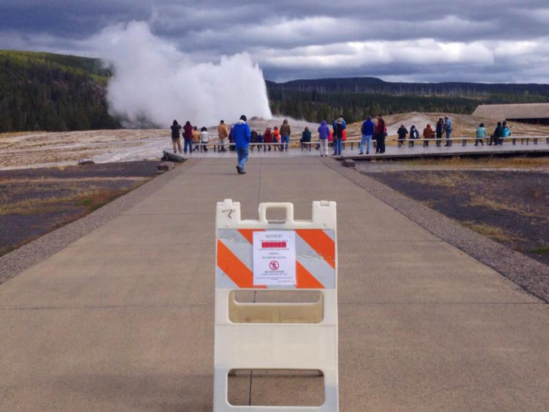 About two dozen visitors to Yellowstone National Park watch Old Faithful Geyser erupt Tuesday afternoon despite a sign advising that the attraction is closed in the wake of a federal goverment shutdown. No visitors were allowed into national parks Tuesday, while those already inside park boundaries will be asked to leave.