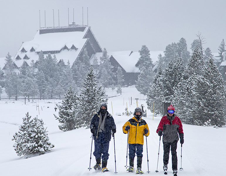 Old Faithful Inn is visible in the background as winter travelers in Yellowstone National Park head out for a trip to Black Sand Pool.